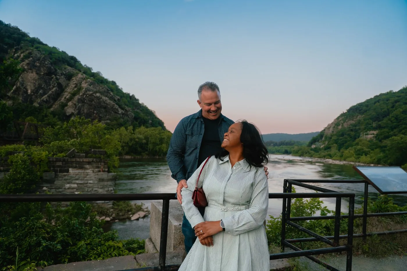 Engaged couple watching the sunset by a river valley