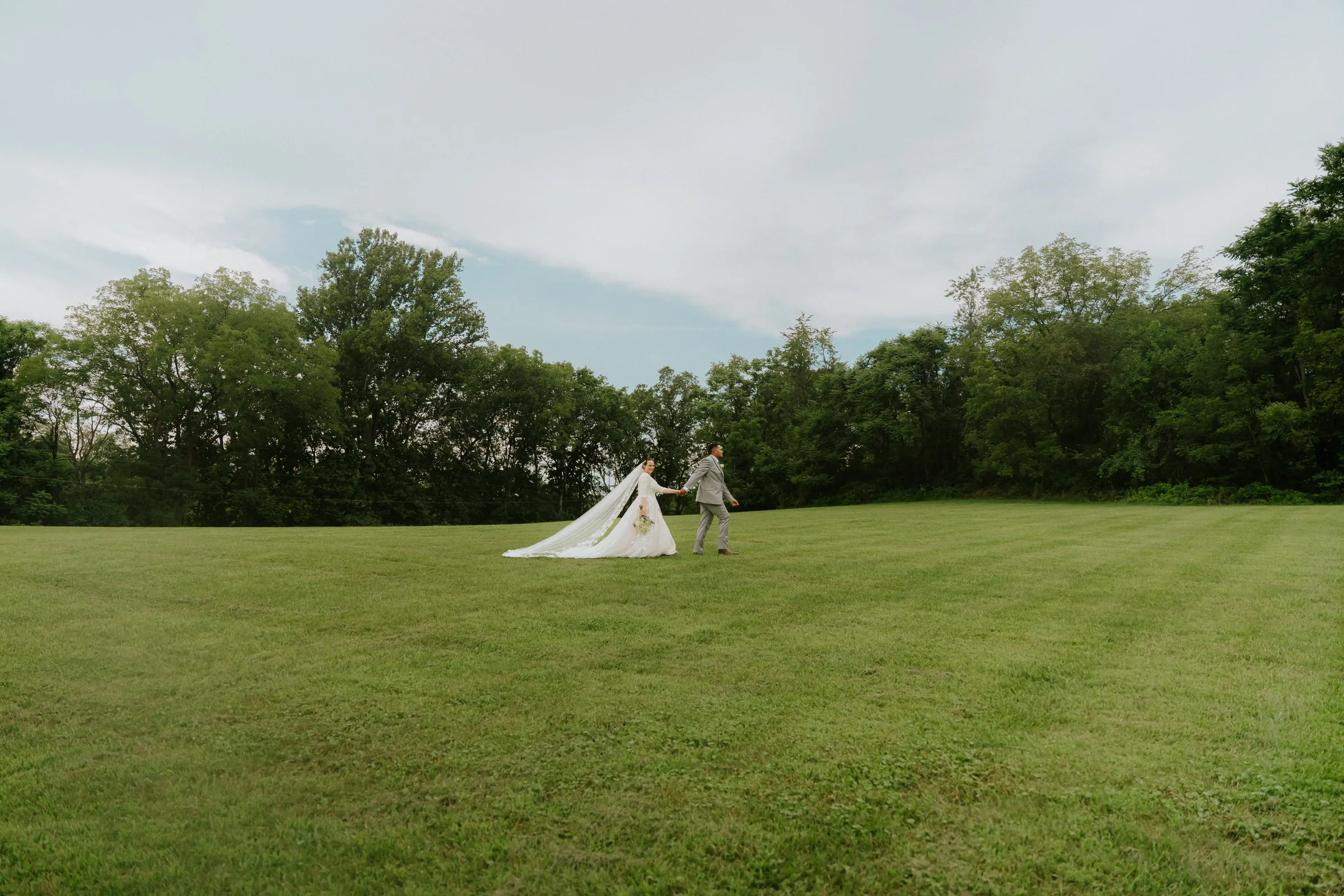 Bride and groom holding hands walking across an open green field